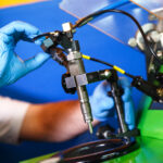 A mechanic wearing blue gloves testing a diesel fuel injector on a diagnostic machine.