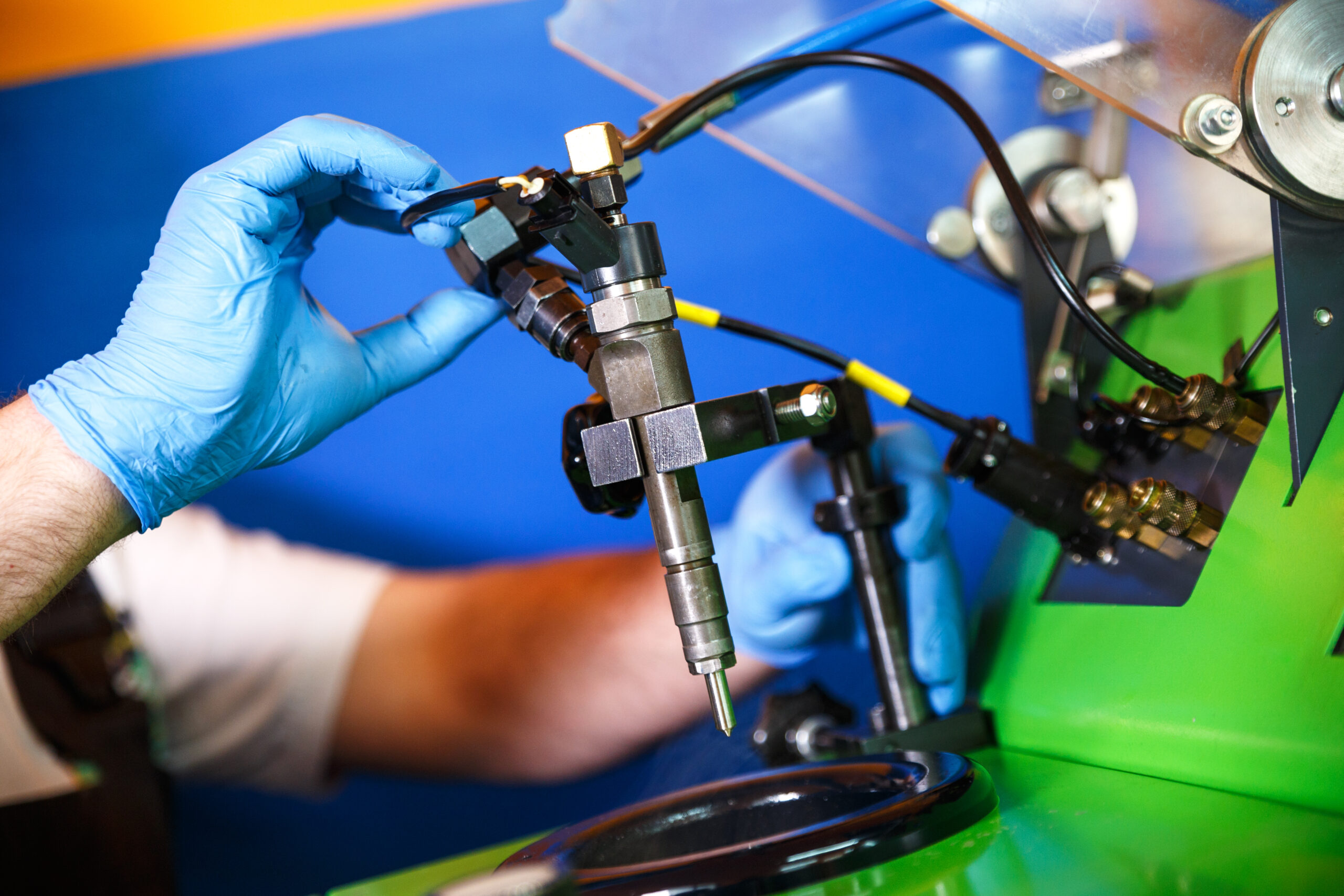 A mechanic wearing blue gloves testing a diesel fuel injector on a diagnostic machine.